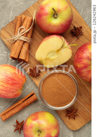 Red apple, cinnamon sticks and cinnamon in bowl on grey concrete background. Vertical photo Red apple, cinnamon sticks and cinnamon in bowl on grey concrete background. Vertical photo 126242963