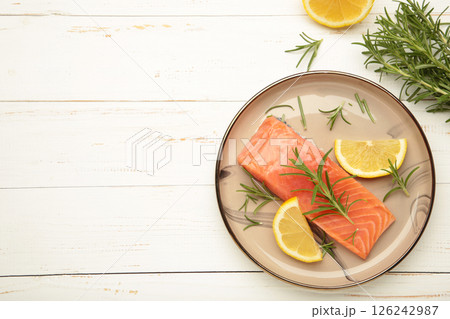 Red fish. Raw salmon fillet with rosemary and lemon on grey plate on white background. 126242987