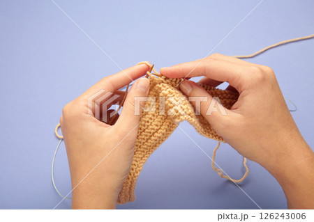 Women's hands knitting. Beige knitting yarns on violet background. 126243006