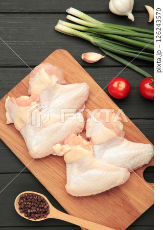 Raw chicken wings with ingredients for cooking on wooden cutting board on black wooden background. Vertical photo 126243570
