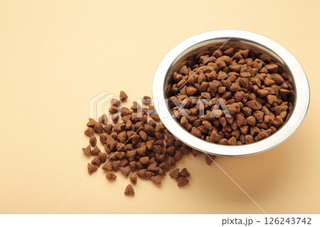 Dog or cat dry food in a silver bowl on beige background. Space for text 126243742