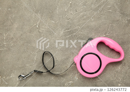 Pink plastic durable and ergonomic leash roulette for pets on grey concrete background. Convenient mechanical device for keeping and controlling dog in street. 126243772