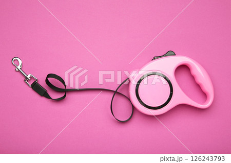 Pink plastic durable and ergonomic leash roulette for pets on pink background. Convenient mechanical device for keeping and controlling dog in street. 126243793