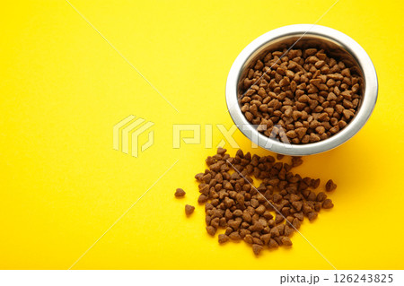 Dog or cat dry food in a silver bowl on yellow background. Space for text Dog or cat dry food in a silver bowl on yellow background. Space for text 126243825