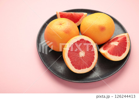 Whole grapefruit with slice on dark plate on pink background. Whole grapefruit with slice on dark plate on pink background. 126244413