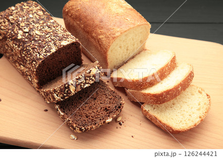 Different bread on cutting board on dark wooden background. 126244421