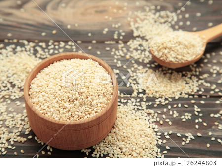 Raw sesame seeds in wooden bowl and spoon on brown wooden background. 126244803