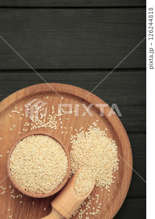 Raw sesame seeds in wooden bowl and spoon on black wooden background. Raw sesame seeds in wooden bowl and spoon on black wooden background. 126244818