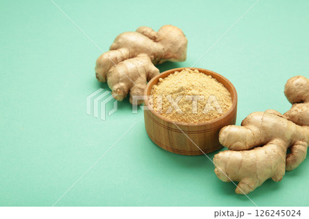 Wooden spoon with dried ginger powder and fresh ginger root on mint background. Top view Wooden spoon with dried ginger powder and fresh ginger root on mint background. Top view 126245024