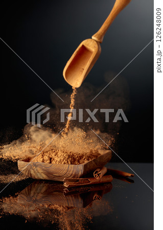 Cinnamon powder is poured into a wooden dish. 126248009