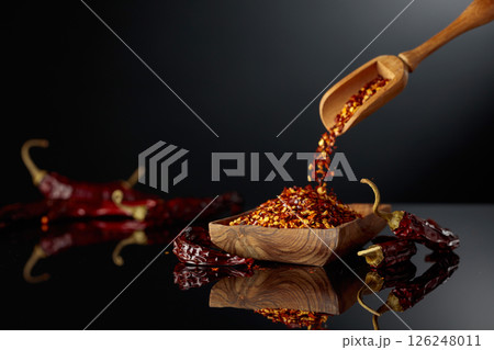 Dry red chili peppers and crushed chili flakes on a black reflective background. 126248011