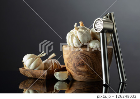 Garlic bulbs and garlic press on a black background. 126248032