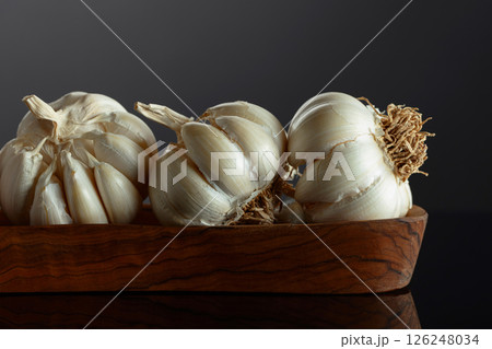 Garlic bulbs in wooden dish on a black background. 126248034