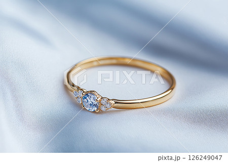 Elegant golden ring featuring a single brilliant cut diamond, placed on a light textured surface. Symbolizing love, commitment, and luxury, this piece highlights the sophistication of fine jewelry. Elegant golden ring featuring a single brilliant cut diamond, placed on a light textured surface. Symbolizing love, commitment, and luxury, this piece highlights the sophistication of fine jewelry. 126249047