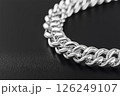 Closeup of a shining silver chain on a textured dark background. Elegant silver chain captured in a detailed closeup with bright lighting on plain blue background. 126249107