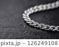 Closeup of a shining silver chain on a textured dark background. Elegant silver chain captured in a detailed closeup with bright lighting on plain blue background. 126249108