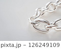Closeup of a shining silver chain on a textured light background. Elegant silver chain captured in a detailed closeup with bright lighting on plain blue background. 126249109