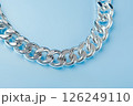 Closeup of a shining silver chain on light background. Elegant silver chain captured in a detailed closeup with bright lighting on plain blue background. 126249110
