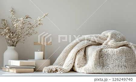 Cozy still life with knitted blanket, candle, wooden cross, books and dried flowers in vase, styled in neutral tones for peaceful and serene atmosphere 126249740
