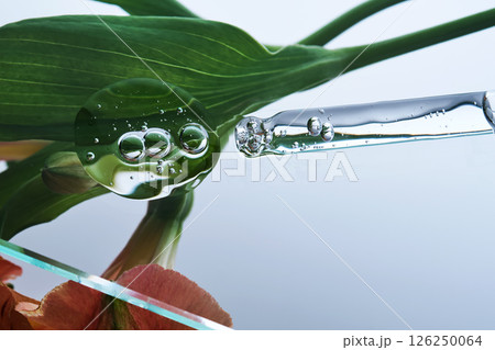 A pipette with a beautiful drop of serum on a background of lily flowers. A pipette with a beautiful drop of serum on a background of lily flowers. 126250064
