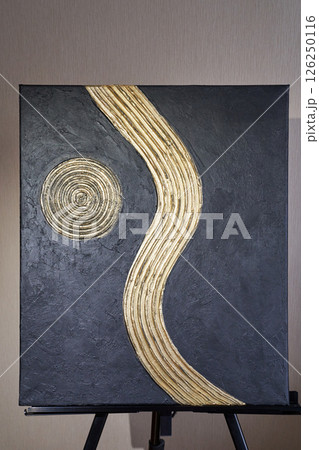 Abstract black canvas with gold spiral and wavy line artwork on easel Abstract black canvas with gold spiral and wavy line artwork on easel 126250116
