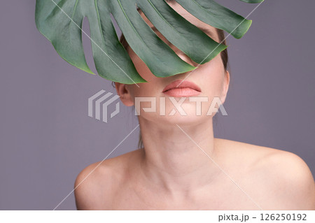 Young caucasian female partially covered by monstera leaf with neutral 126250192