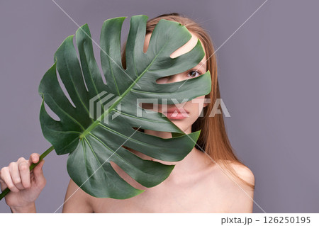 Young caucasian female partially covered by large green leaf against gray 126250195