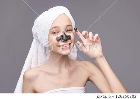 Young caucasian female applying charcoal face mask with towel wrapped hair 126250202