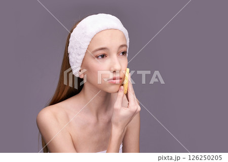 Young caucasian female using facial cleansing tool for skincare routine on gray 126250205