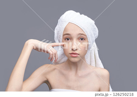 Young caucasian female with under eye patches and towel turban on gray Young caucasian female with under eye patches and towel turban on gray 126250218