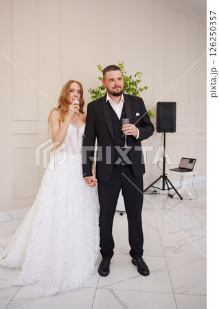 The bride and groom stand in the banquet hall listen to the toasts of the guests The bride and groom stand in the banquet hall listen to the toasts of the guests 126250357