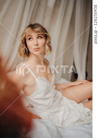 Beautiful young woman in a white dress on white sheets Beautiful young woman in a white dress on white sheets 126250438