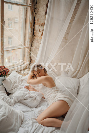 an attractive blonde woman in a white dress on white sheets 126250456