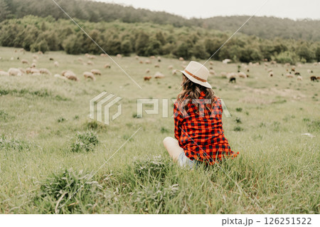 A woman sits in a field of grass with a hat on 126251522