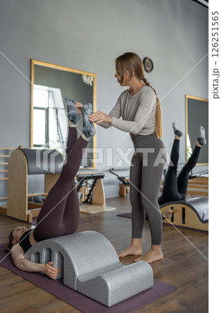 Group of women doing exercises on back spine corrector. Reformer pilates studio machine for fitness workouts in gym. Fit, healthy and strong authentical body. Fitness concept. Group of women doing exercises on back spine corrector. Reformer pilates studio machine for fitness workouts in gym. Fit, healthy and strong authentical body. Fitness concept. 126251565