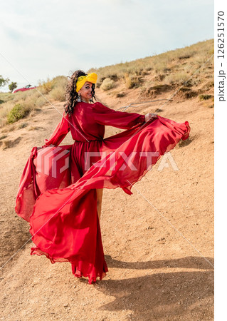 A woman in a red dress is posing for a photo on a dirt road. She is wearing a yellow headband and has her arms outstretched. Concept of freedom and joy. A woman in a red dress is posing for a photo on a dirt road. She is wearing a yellow headband and has her arms outstretched. Concept of freedom and joy. 126251570