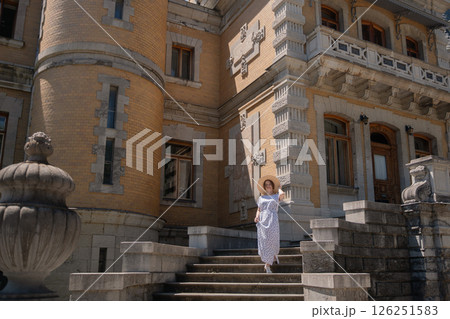 A woman in a white dress stands on a set of stairs in front of a large building 126251583
