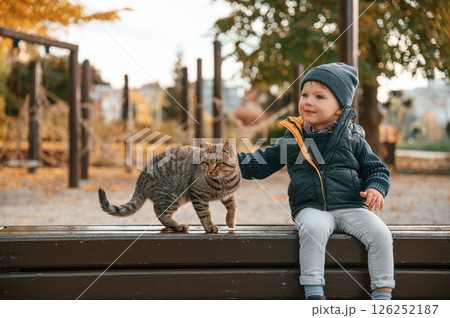 Young boy is sitting on the bench with cute cat outdoors 126252187