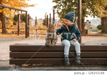 Young boy is sitting on the bench with cute cat outdoors 126252188