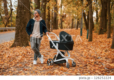 Enjoying the nature. Man with pram is having a walk in the autumn park Enjoying the nature. Man with pram is having a walk in the autumn park 126252224