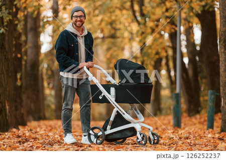 Standing and enjoying a nature. Man with pram is having a walk in the autumn park Standing and enjoying a nature. Man with pram is having a walk in the autumn park 126252237