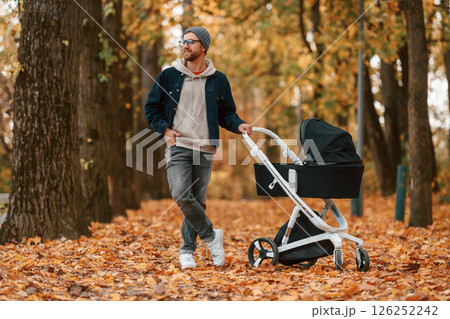 Standing and enjoying a nature. Man with pram is having a walk in the autumn park 126252242