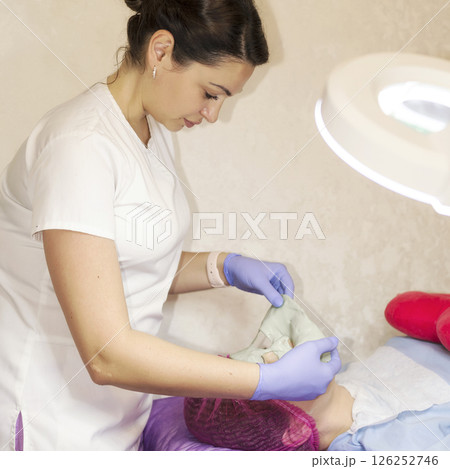 A female cosmetologist doctor makes a facial mask for a client 126252746