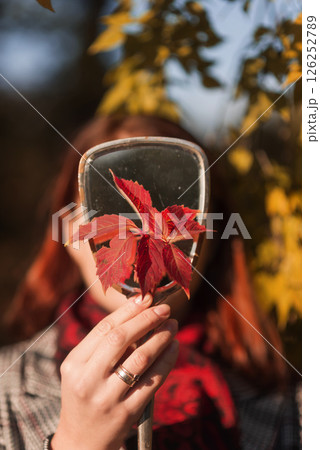 female hand holding mirror and autumn red leaf 126252789
