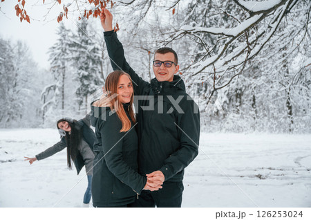 Man touching branch, woman is having fun behind the. Couple is in the winter forest, having a walk 126253024