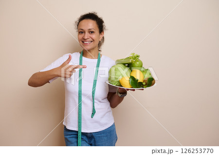 Smiling Woman Promoting Healthy Eating with Fresh Fruits and Vegetables for Weight Loss and Wellness 126253770