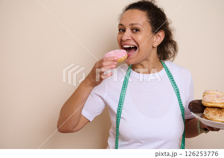 Woman Enjoying Donuts with a Measuring Tape Highlighting a Fun Take on Balancing Diets and Treats Woman Enjoying Donuts with a Measuring Tape Highlighting a Fun Take on Balancing Diets and Treats 126253776