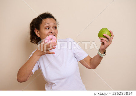 Woman Deciding Between a Sweet Doughnut and a Fresh Green Apple Woman Deciding Between a Sweet Doughnut and a Fresh Green Apple 126253814