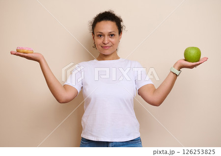 Smiling Woman Choosing Between a Healthy Green Apple and a Sugary Doughnut 126253825