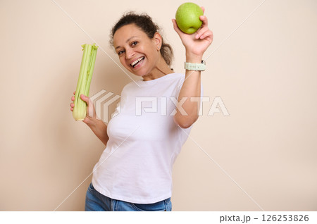 Smiling Woman Promoting Healthy Lifestyle with Apple and Celery Smiling Woman Promoting Healthy Lifestyle with Apple and Celery 126253826
